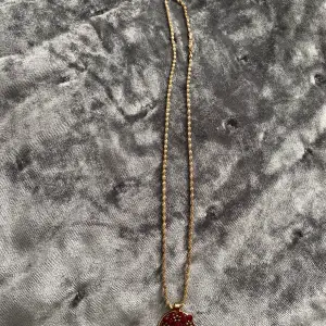 Ett fint guld halsband med en vinröd blomma
