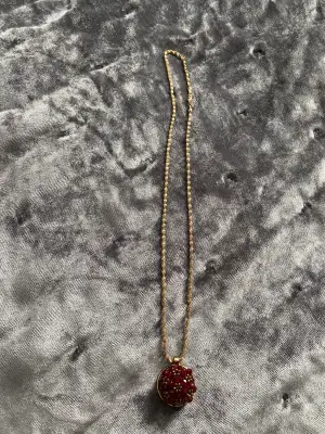 Ett fint guld halsband med en vinröd blomma