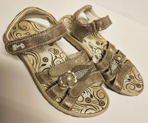 Sandaler från Primigi  - Guldiga sandler från Primigi. Använda under några tillfällen en sommar, fint skick. Har inte försökt tvätta dem utan de säljs i befintligt skick och går säkert att piffa till mer. Har en "shock absorber" sula.  Storlek 33. Nypris 600 kr. 