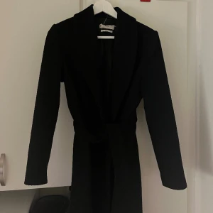 Svart lång kappa från mango i ullblandning - Köpt för två år sen på mango, använd men fint skick.  Snygg att ha både med eller utan band (finns knapp framtill) varm och tung kappa så passar perfekt till vinter.  Går ner till vaderna på mig som är 170 cm.  Köpt för 1800kr