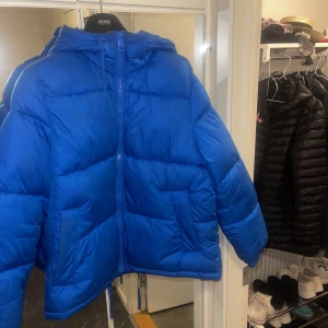Pufferjacket trendig blå från Hm - Säljer min blåa, stora och mysiga vinterjacka. Nypris 550kr.Jackan är varm och fluffig, den har stora fickor samt snören som går att dra åt i både luvan & längst ned på jackan.Perfekt för den som vill ha en varm & mysig vinterjacka. Har stoppning i luvan.