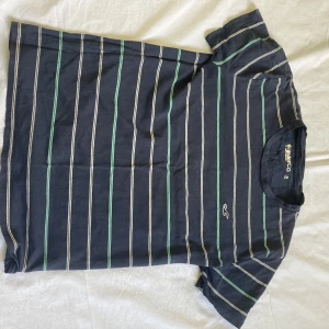 Randig Holister T-shirt.  - Randig holister T-shirt i storlek XS. Har en regnbågsfärgad cirkel som är broderat på vänstra ärmen