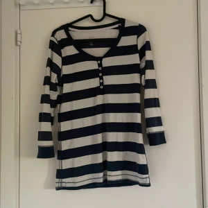 Lång ärmad tröja - Den är i storlek M och är ifrån H&M! Den är randig med tjocka ränder och är i färgen blå/svart och vit. Trådar från sömmen är lite slitna och sticker ut lite men det går lätt att fixa med en sax✂️ knappar på framsidan också.🤍 köp gärna🤍V ringad vid halsen.