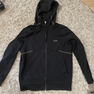 Hugo boss zip hoodie (guld och svart) - Den är liten i storleken ja brukar ha storlek m men körde l på denna. Annars fint skick inga skador. På bilden är de några prickar men de bara damm