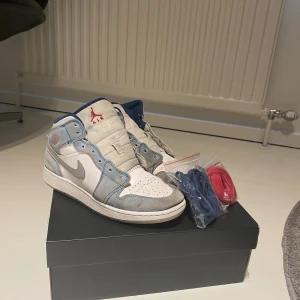 Jordan 1 mid dusty blue - Ett par begagnade Jordan 1 mid som kommer med vita snören, blåa ochröda. Du får med boxen. Det är storlek 40. Skorna i nypris går från 2000-3000 beroende på. 