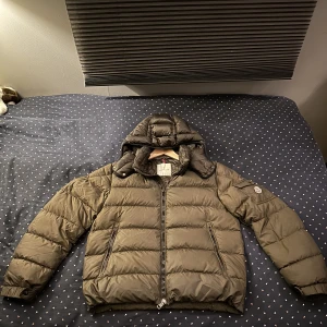 Moncler vinter jacka  - Jag säljer en Moncler vinter jacka i färgen mörkgrön. Jackan har inga fläckar eller skador på utsidan. På insidan finns det ett litet hål i armvecke, syns dock ej på utsidan. Tecknade serien sitter lite löst. Dragkedjan fungerar bra, dock en bit borta ❤️