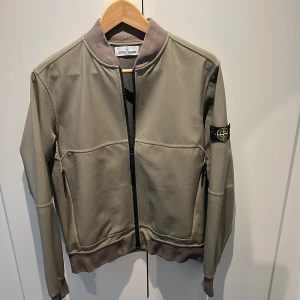 Stone Island jacka - junior - Stone Island jacka storlek 14/170. Färgen är oliv/grå, mudd vid ärmslut, midjan och vid hals. Svart dragkedja framtill, dolda fickor med drajkedja i sidorna. I mycket gott skick!  Inköpt på NK barnavdelning för några år sedan, kvittot ej kvar.