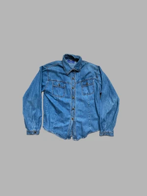 Jeansskjorta  - Fin jeansskjorta i mediumljus tvätt. Köpt i Köpenhamn för flera år sedan och nu behöver den hitta en ny garderob. 100% bomull. Storlek S skulle kunna passa M.