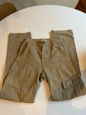 Cargo byxor i beige/brun - Säljer mina cargo byxor från stradivarius i storlek 32. Modellen är bred och high waist. Den är knappt använd och i ny skick. Den har fickor på båda sidor av benen. 