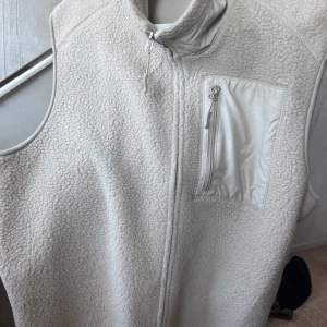 HM väst - En beige HM väst med en framficka. Västen är i fint skick, knappt använd pga storlek. Nypris: 450kr. Priset är fast.  Skick: 10/10 (aldrig använd)