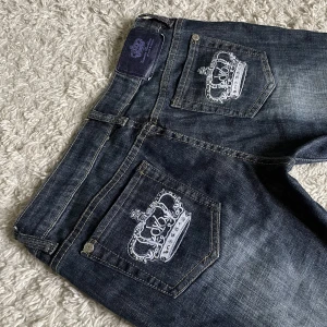 Vintage Victoria Beckham jeans - Lågmidjad och bootcut modell med vita kronor och rhinestones på bakfickorna (OBS en del har låstnat!)❤️ Innerben: 78-79cm, midja rakt över: 40,5cm. Jag är 165cm som referens, kan fixa fler mått! 🫶 Håll koll på min profil, lägger ofta upp vintage jeans! 😍