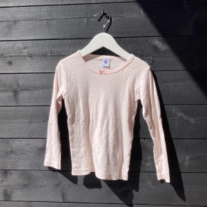 Ljusrosa tröja - En puderrosa tröja med en liten rosett på halslinningen.