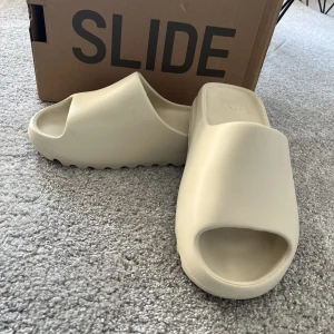 Yeezy Slide - Hej, säljer mina yeezy Slides i storlek 42 då dem inte passar längre. Skicket är 10/10 Färgen är bone white