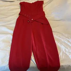Röd byxdress i storlek 34 med ett bälte. 