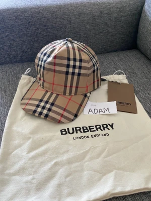 BURBERRY KEPS NYASTE MODELLEN - Mycket fin stilren BURBERRY keps av färgen beige med prislapp, den nyaste modellen på marknaden! Hör av dig vid intresse!