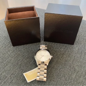 Michael Kors klocka  - Säljer äkta Michael Kors klocka i silver. Aldrig använd, prislapp kvar. Priset kan diskuteras vid en snabb affär. Köparen står för fraktkostnader. Box ingår. Nypris: 1995kr