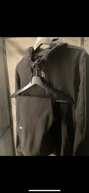 Moose knuckles  - Ny Dundas luvtröja och byxor med dragkedja framtill från MOOSE KNUCKLES svart, bomull, svartfärgad logotypplakett, huva med dragsko, dragkedja framtill, långa ärmar, två sidfickor och ribbade ärmslut och fåll.