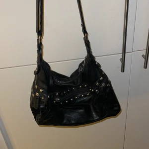 Väska - Väska med ställbart band och med silvriga detaljer. Mycket bra väska med många fack, både på insidan och utsidan. I mycket gott skick 