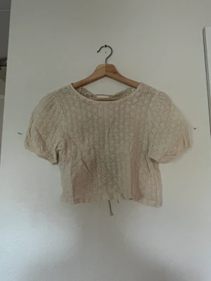 Topp - Beige blus med mönster och knyte baktil. Storlek XS.