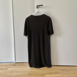 Svart t-shirt klänning - En superfin svart t-shirt klänning/tunika i glansigt ribbat tyg. Den är lite genomskinlig men man kan ha shorts under! Köpt via Sellpy men den är från Gina Tricot. I fint skick!
