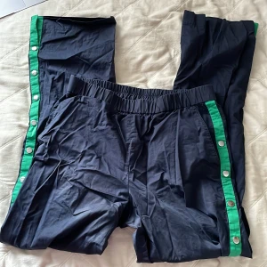 Knappade byxor - Säljer dessa byxor i överdrags-aktigt material. De har coola gröna detaljer med knappar på sidorna. Storlek samt märke saknas, men de passar mig som har storlek S, eller om du vill ha dem lite mer baggy så funkar de även för Xs.  Köpare står för frakt!