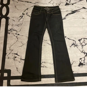 Lågmidjade bootcut jeans  - Säljer ett par blåa lågmidjade bootcut jeans med snyggt mönster på bakre fickorna. Materialet på jeansen är inte stretchigt men i mycket bra skick på grund av att det aldrig har används men dock är knappen lite lös men inget som hindrar än från att ha på.