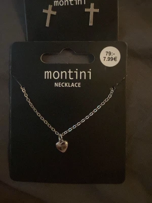 Silverfärgat halsband med hjärthänge och örhängen - Snyggt silverfärgade korsörhängen och hjärthalsband från Montini med ett litet hjärthänge. Kedjan är tunn och stilren, perfekt för att ge en söt touch till din outfit. Halsbandet är enkelt att matcha med andra smycken och har en klassisk design. Smyckena är även helt oanvända.
