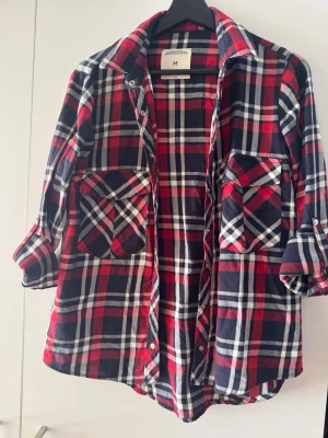Rutig skjorta från Zara Woman - Säljer en röd, blå och vit rutig skjorta från Zara Woman. Skjortan har långa ärmar, två stora bröstfickor och klassisk krage. Perfekt för dig som gillar en avslappnad och trendig stil.