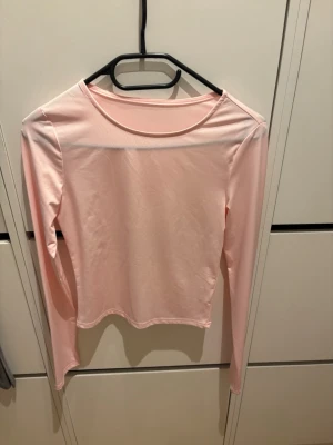 Ljusrosa långärmad topp i polyester - Säljer en ljusrosa långärmad topp i mjukt och stretchigt material. Toppen har en enkel och clean design med rund halsringning och figurnära passform. Perfekt att styla med jeans eller kjol för en fräsch look.