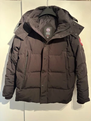 Svart dunjacka med huva Canada Goose - Canada Goose jacka i mycket bra skick. Sparsamt använd och i mycket fint skick utan större märken eller skador.  Det enda att anmärka på är att sömmen som delar upp ena framfickan i två delar har gått upp. Fickan är därför numera en stor ficka istället för två mindre, men den fungerar precis som vanligt och påverkar inte jackans funktion.  Originaltillbehör medföljer, inklusive Canada Goose-påse, tags/lappar samt avtagbar päls.  Säljes då jag inte längre använder den.