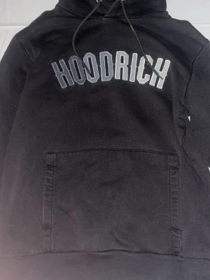 Svart Hoodrich loungewear set - Säljer ett svart loungewear set från Hoodrich med matchande hoodie och byxor. Hoodien har stor magficka och dragsko i huvan, samt Hoodrich-logga i vitt på bröstet. Byxorna har resår i midjan och logga på ena benet. Perfekt för chill dagar hemma.