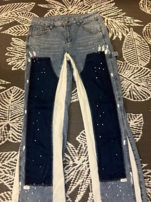 Unika blå och vita jeans från Romwe - Säljer ett par riktigt coola jeans från Romwe med kontrasterande mörkblå och vita paneler längs benen. Jeansen har en relaxed fit, vita färgstänk och detaljer som sticker ut. Perfekta för dig som vill ha något annorlunda i garderoben!
