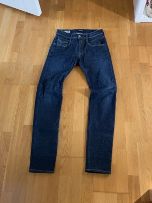 Mörkblå slim fit jeans - Snygga mörkblå jeans i slim fit-modell med klassiska fem fickor och kontrastsömmar. Jeansen har raka ben och detaljerade bakfickor med broderade sömmar. Har lite egengjorda slitage 