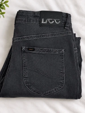 Mörkgråa raka jeans från Lee - Snygga svarta jeans från Lee med rak passform och klassisk femficksdesign. Jeansen har en diskret Lee-logga på bakfickan och är tillverkade i ett mjukt denimtyg som ger en avslappnad look. Perfekta till en streetwear-outfit.