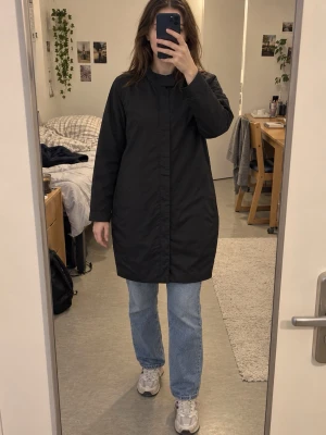 Svart rak rock med dold dragkedja - Säljer en svart rock med rak passform och dold dragkedja framtill. Rocken har långa ärmar och enkel, stilren design utan synliga detaljer. Perfekt för dig som gillar minimalistisk stil och vill ha en klassisk look.