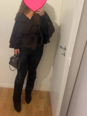 Mörkbrun kappa med knytskärp - Snygg mörkbrun kappa från Gina Tricot med bred krage och knytskärp i midjan. Kappan har en avslappnad passform, knappar framtill och vida ärmar. Perfekt för dig som vill ha en trendig och stilren look till hösten eller vintern. Storleken är XS-S men funkar för M-L ochså!