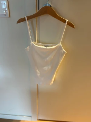 Vit ribbad linnetopp från Kappahl (barn) - Snygg vit ribbad linnetopp från Kappahl med smala axelband. Perfekt att styla med jeans eller kjol för en fräsch look. Toppen är croppad och har en enkel, stilren design som passar till många outfits.