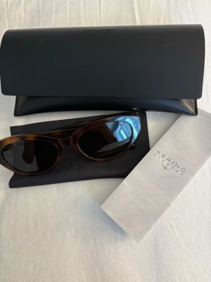 Saint Laurent bruna cat eye solglasögon - Trendiga solglasögon från Saint Laurent i brunsköldpaddsmönstrad plast med cat eye-form. Mörka linser och silverfärgad YSL-logga på skalmen. Kommer med originalfodral och putsduk, perfekt för dig som vill ha en lyxig accessoar.