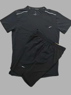 Svart träningsset med t-shirt och shorts - Säljer ett svart träningsset med kortärmad t-shirt och matchande shorts. Setet har diskreta vita detaljer och är gjort i ett lätt, snabbtorkande material som passar perfekt för löpning eller gym. T-shirten har rund hals och shortsen har resår i midjan.