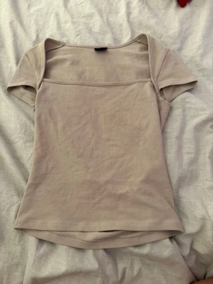 Beige kortärmad topp med fyrkantig ringning - Snygg beige topp med korta ärmar och fyrkantig ringning. Tillverkad i mjuk bomull som känns skön mot huden. Enkel och stilren design som passar till det mesta. Perfekt för dig som gillar minimalistisk stil.