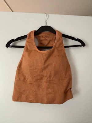 Orange sport-bh/topp - Snygg orange sport-bh med meshdetaljer för extra ventilation. Inbyggda kupor. Tillverkad i ett stretchigt funktionsmaterial som andas. Perfekt för träning och ger bra stöd. Brottarrygg och bred resår under bysten för skön passform. Står storlek M men sitter som en XS. Knappt använd. 