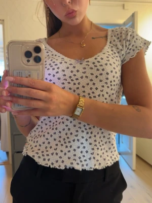Vit topp volang - Söt vit topp med volangkant nertill och vid ärmslut. Toppen har en liten rosett vid urringningen och korta ärmar. Perfekt för dig som gillar gulliga detaljer och en feminin stil.