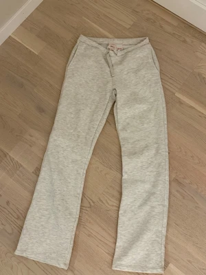 Ljusgråa lowwaist raka mjukisbyxor - Säljer ett par ljusgrå mjukisbyxor med raka ben och resår i midjan. Byxorna har två sidofickor och är tillverkade i ett mjukt och bekvämt material, perfekt för en avslappnad stil.