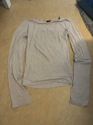 Ljusbeige långärmad topp - En enkel och stilren ljusbeige långärmad topp i mjukt material. Perfekt att matcha med jeans eller kjol för en clean look. Toppen har rund halsringning och normal passform.