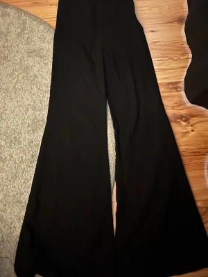 Svarta utsvängda kostymbyxor Interco - Svarta kostymbyxor från Interco i storlek 34. Byxorna har en hög midja och vida, utsvängda ben för en trendig siluett. Perfekta att styla med en snygg topp eller kavaj. Materialet är mjukt och följsamt.