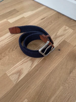 Mörkblått flätat bälte Jack & Jones - Snyggt mörkblått flätat bälte från Jack & Jones med detaljer i brunt skinn och silverfärgat spänne. Perfekt för att lyfta din outfit med en stilren accessoar. Bältet har en klassisk design och passar till många olika looks.