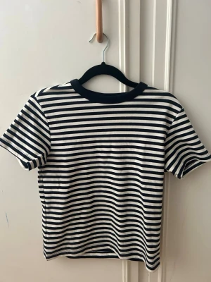 OANDVÄND Randig t-shirt med marin känsla - Snygg t-shirt med svarta och vita horisontella ränder och svart ribbad krage. Klassisk passform och korta ärmar, perfekt till jeans eller kjol. Tillverkad i mjuk bomull för skön känsla hela dagen😚🫐