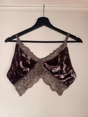 Brun sammetsbralette med spets - Supersnygg bralette i brun sammet med tunna axelband och dekorativ spetskant i beige. Mjuk och stretchig modell utan bygel, perfekt för en avslappnad och trendig look. Materialet är glansigt och ger en lyxig känsla.