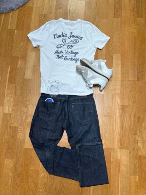 Levi's 501 mörkblå raka jeans - Säljer ett par klassiska Levi's 501 jeans i mörkblå denim med raka ben och fem fickor. Jeansen har den ikoniska röda Levi's-lappen på bakfickan och patch i läder bak i midjan. Perfekta för en avslappnad och tidlös stil. Finns en upprivning på knäet men det är inget hål. Jag har även klippt jeansen där nere så de blir som bootcut. 