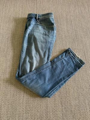 Blå jeans från Diesel - Säljer ett par klassiska blå jeans från Diesel med snygg tvätt och raka ben. Jeansen har fem fickor, bälteshällor och en läderpatch med Diesel-loggan bak i midjan. Perfekta för en avslappnad och trendig stil.